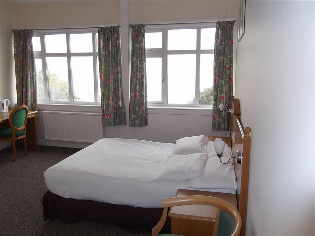 Habitación de hotel con cama, escritorio, silla y ventana con cortinas.