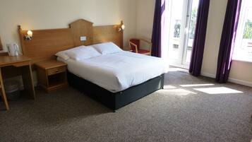 A hotel room with a bed, bedside table, lamp, and a view of the outdoors.