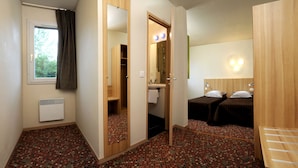 A hotel room with a large mirror, a window with curtains, a shower, a sink, two beds, and a patterned floor.