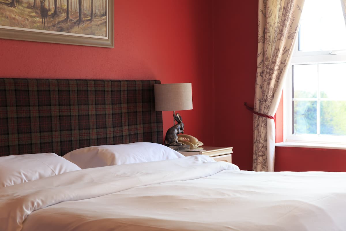 A neatly made bed with white linens, a plaid headboard, a lamp, and a telephone on a bedside table.