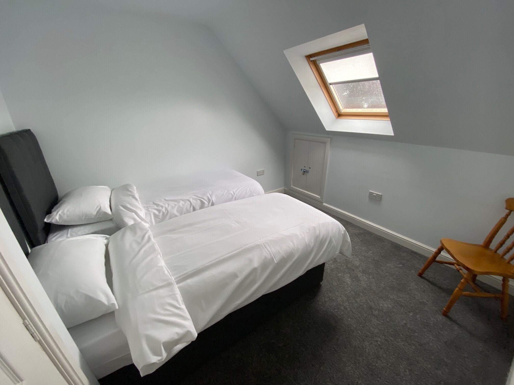 A bedroom with a bed, a chair, a wardrobe, and a skylight.