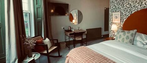 Quarto de hotel com uma cama grande, escrivaninha, cadeira, televisão e janela com cortinas.