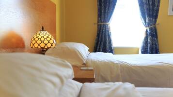 A hotel room with two beds, a bedside table with a lamp, and a window with curtains.