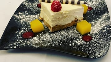 A dessert on a square plate with powdered sugar, a raspberry, and a slice of banana.