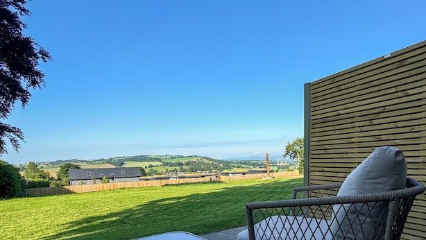 A patio with a table and a wicker chair, overlooking a green landscape and distant hills. - Pilgrim Hotel (Hereford)