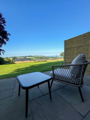 A patio with a table and a wicker chair, overlooking a green landscape and distant hills. - Pilgrim Hotel (Hereford)