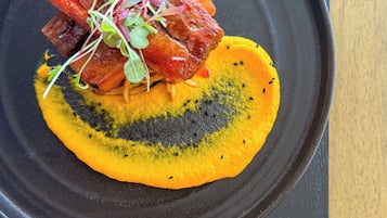 Un piatto nero con un piatto di cibo, tra cui sembra esserci carne e una fetta di frutto giallo, forse un mango, su un tavolo di legno.