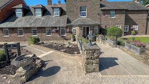 A stone building with multiple windows and a garden area with a bird bath and flower beds. - Pilgrim Hotel (Hereford)