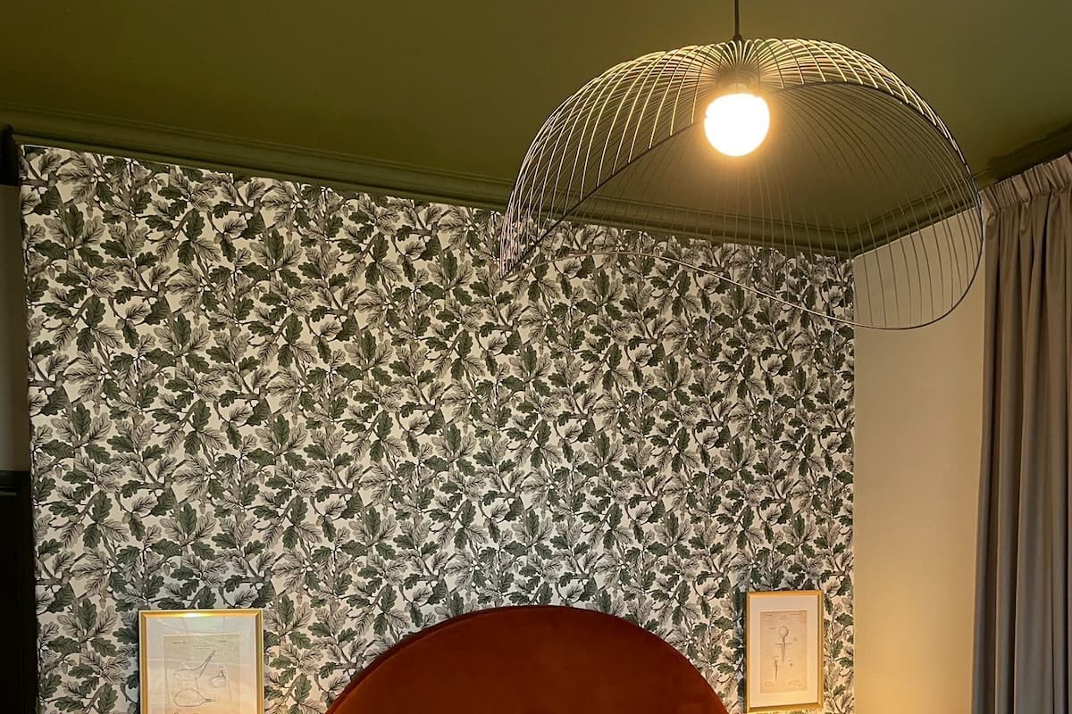 A hotel room with a large bed, two bedside lamps, a telephone, and a wall with a leafy pattern.