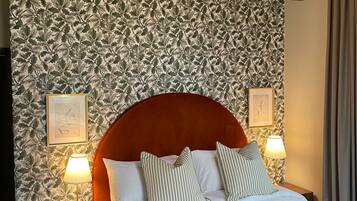 A hotel room with a large bed, two bedside lamps, a telephone, and a wall with a leafy pattern.