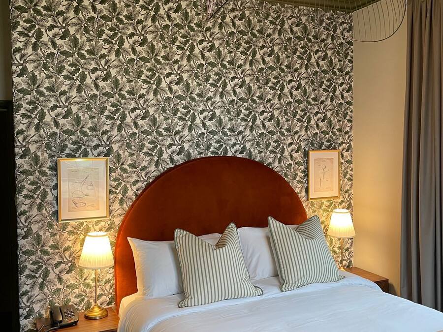 A hotel room with a large bed, two bedside lamps, a telephone, and a wall with a leafy pattern.
