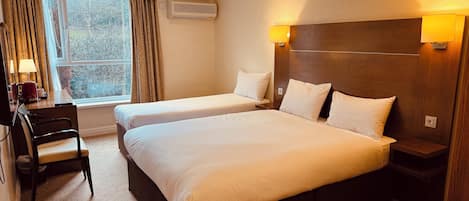 A hotel room with two beds, a desk, a chair, a lamp, and a window with curtains.