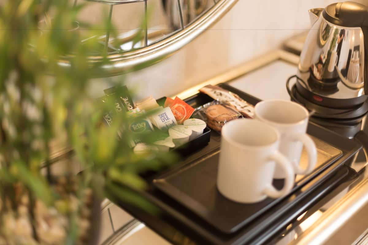 A tray with a coffee maker, two white mugs, and a selection of snacks and beverages.
