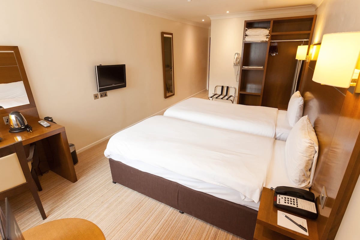 A hotel room with a large bed, a desk with a telephone, a TV, and a wardrobe.