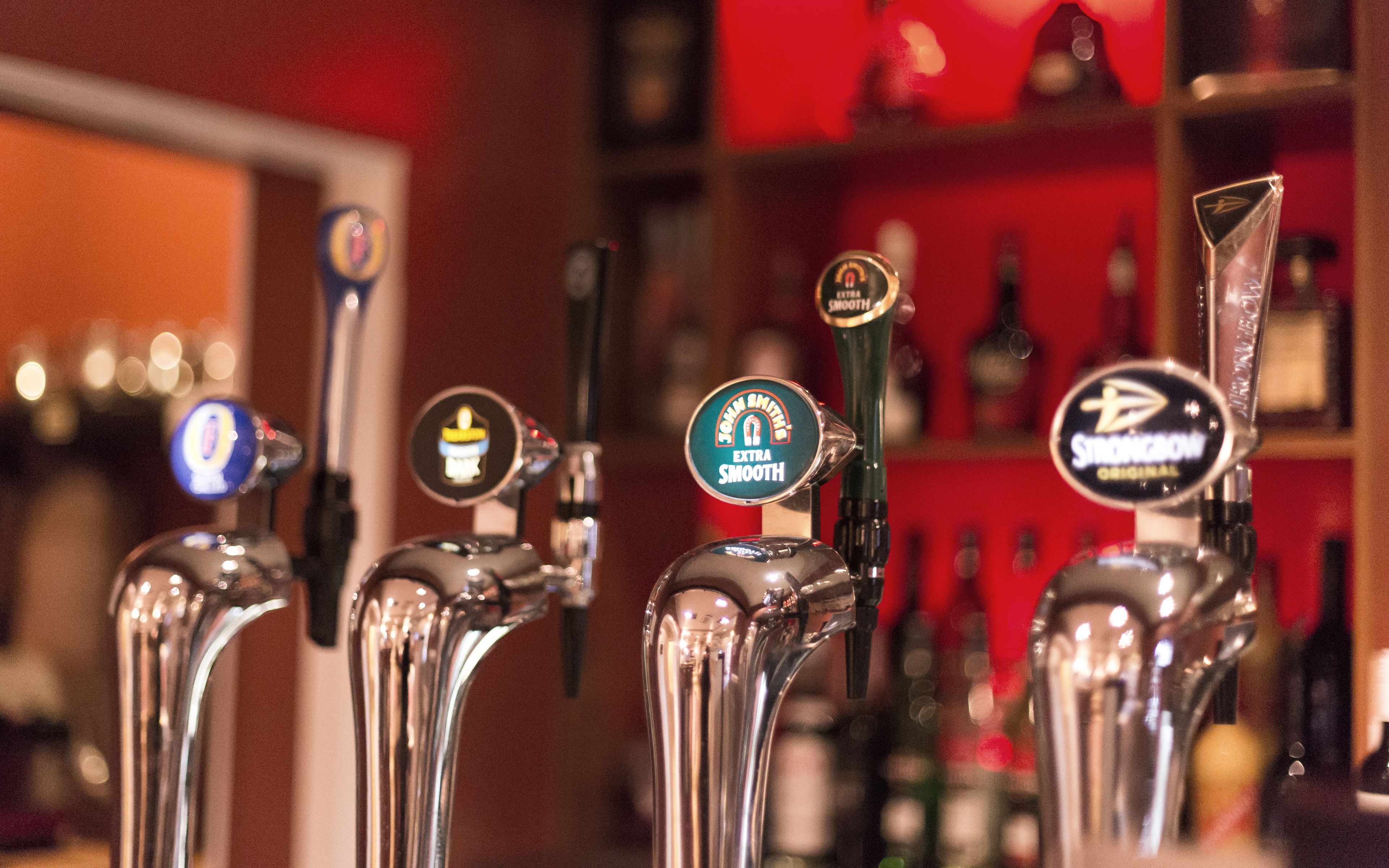 A row of bar taps with labels such as "John Smith's Extra Smooth" and "Strawberry Bourbon."