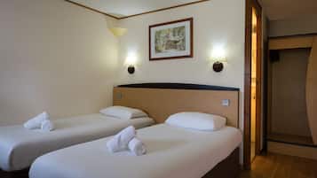 Een hotelkamer met twee enkele bedden, elk voorzien van een opgerolde handdoek, een houten hoofdbord en twee wandlampen.