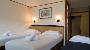 A hotel room with two beds, each with white linens and towels, a wooden headboard, and wall-mounted lamps.