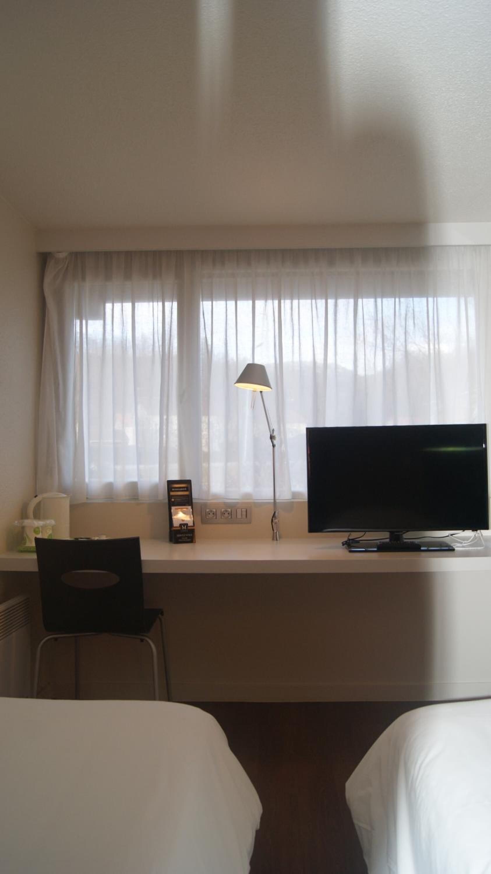 Een hotelkamer met een bed, een bureau met een scherm, een lamp en een stoel.