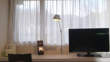 Een hotelkamer met een bed, een bureau met een scherm, een lamp en een stoel.