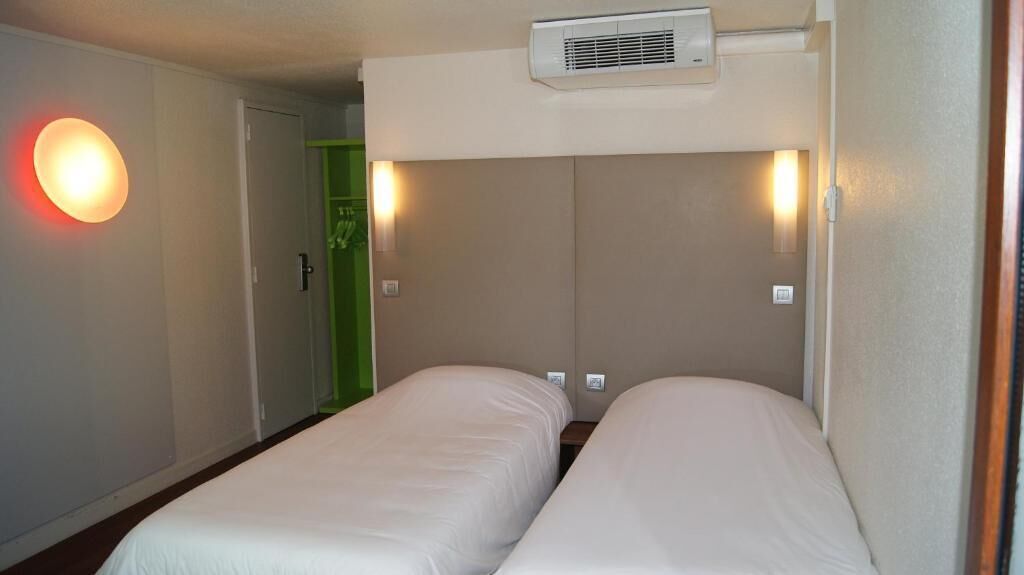 Habitación de hotel con dos camas individuales, aire acondicionado de pared y una puerta con marco verde.