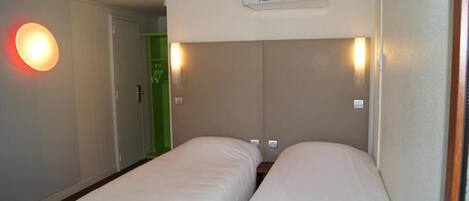 Habitación de hotel con dos camas individuales, aire acondicionado de pared y una puerta con marco verde.