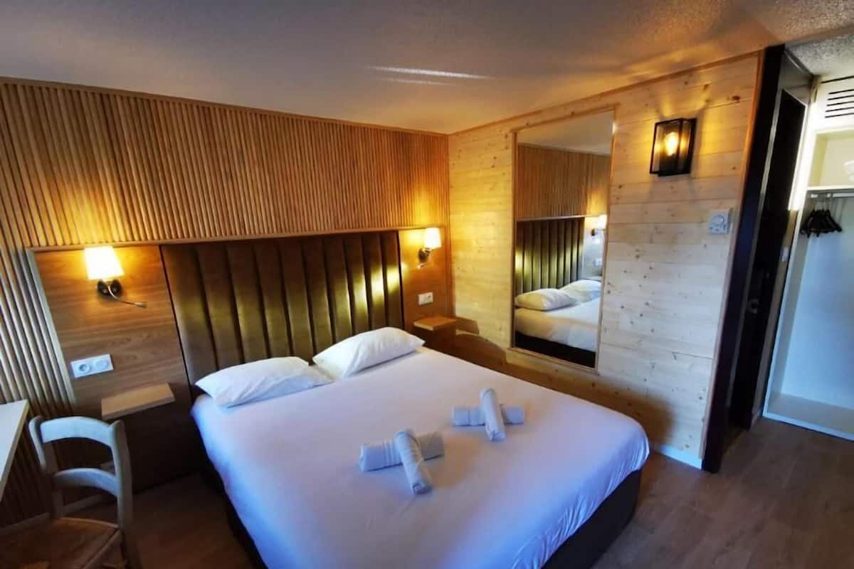 A hotel room with a large bed, two bedside lamps, a wooden headboard, a mirror, and a desk with a chair.