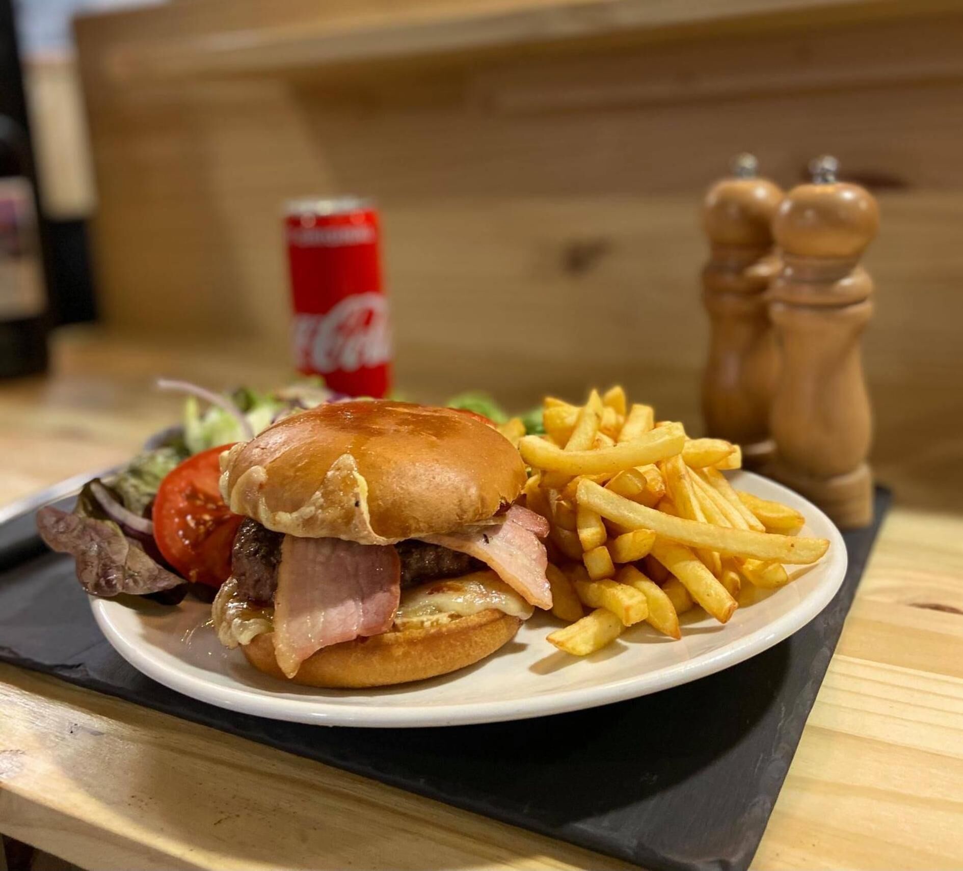 Eine Mahlzeit bestehend aus einem Burger mit Speck, Pommes Frites, einem Salat und einer Flasche Coca-Cola.