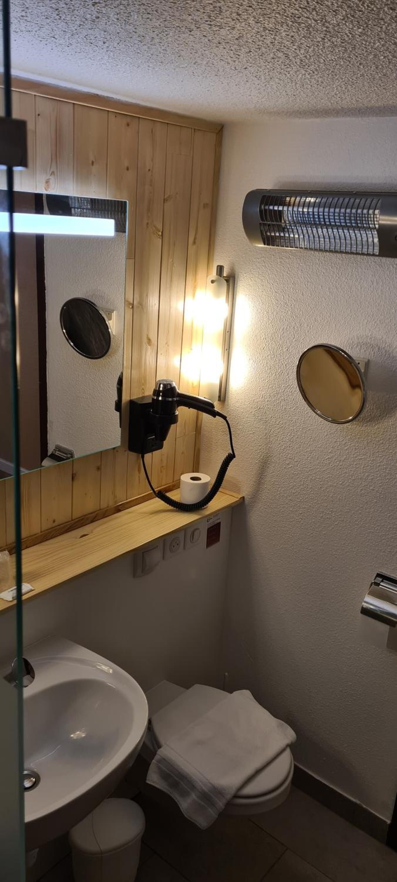 Ein kleines Badezimmer mit einem Holzlagerfläschchen, einem Spiegel, einem Waschbecken, einer Toilette und einem Handtuchhalter.