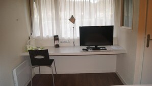 Una pequeña oficina privada con un escritorio, un monitor de computadora, una silla, una lámpara y una ventana con cortinas.
