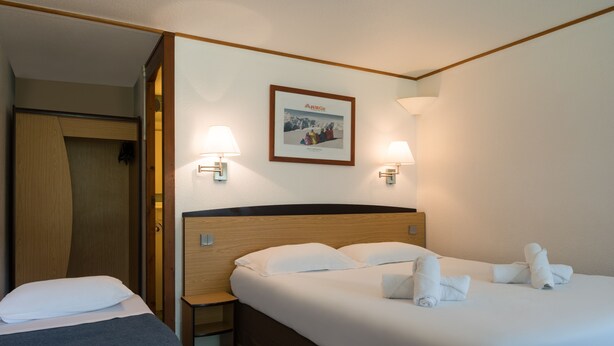Habitación de hotel con dos camas, cabecero de madera, un cuadro enmarcado en la pared y dos lámparas fijadas a la pared.
