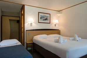 A hotel room with two beds, a wooden headboard, a framed picture on the wall, and two wall-mounted lamps.