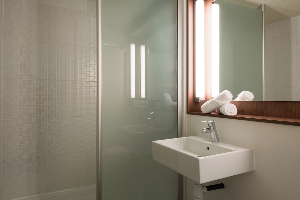 A modern bathroom with a glass shower enclosure, a white sink, and a mirror with vertical light fixtures.