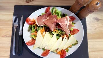 A plate of food with a salad, prosciutto, and cheese on a black placemat.