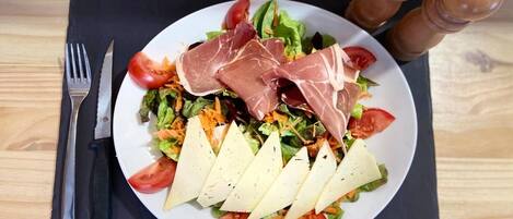 A plate of food with a salad, prosciutto, and cheese on a black placemat.
