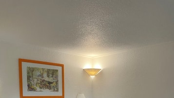 A neatly made bed with white linens, a headboard, a wall-mounted lamp, and a framed picture on the wall.