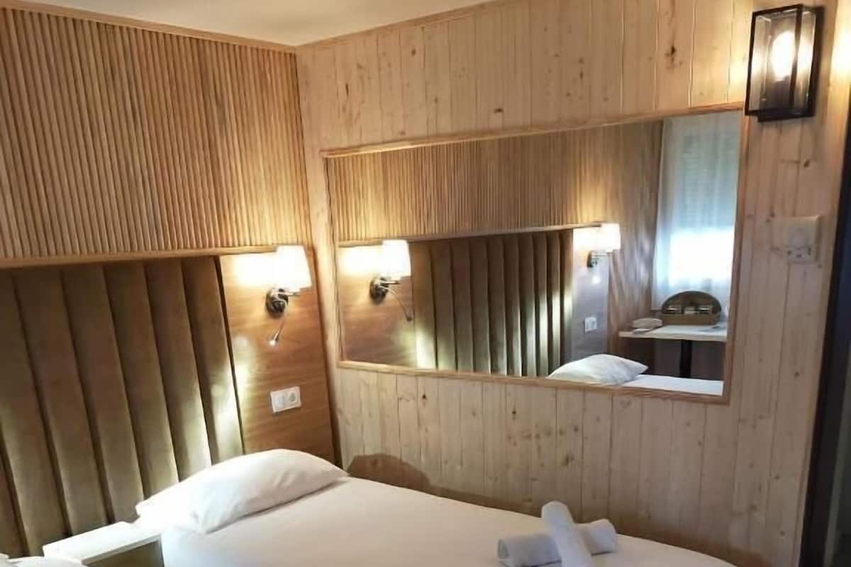 A hotel room with two beds, wooden paneling, a mirror, and a small table.