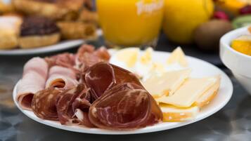 A plate of cured meats and cheese, a glass of orange juice, and a bowl of fruit on a table.
