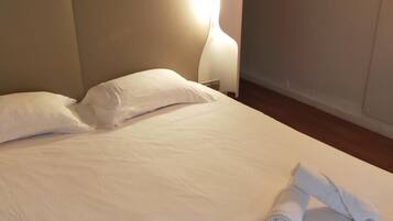 A hotel room with a bed, pillows, and a rolled towel on the bed.