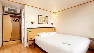 Habitación de hotel con una cama de madera, una mesita de noche, un armario y dos luces fijadas a la pared.