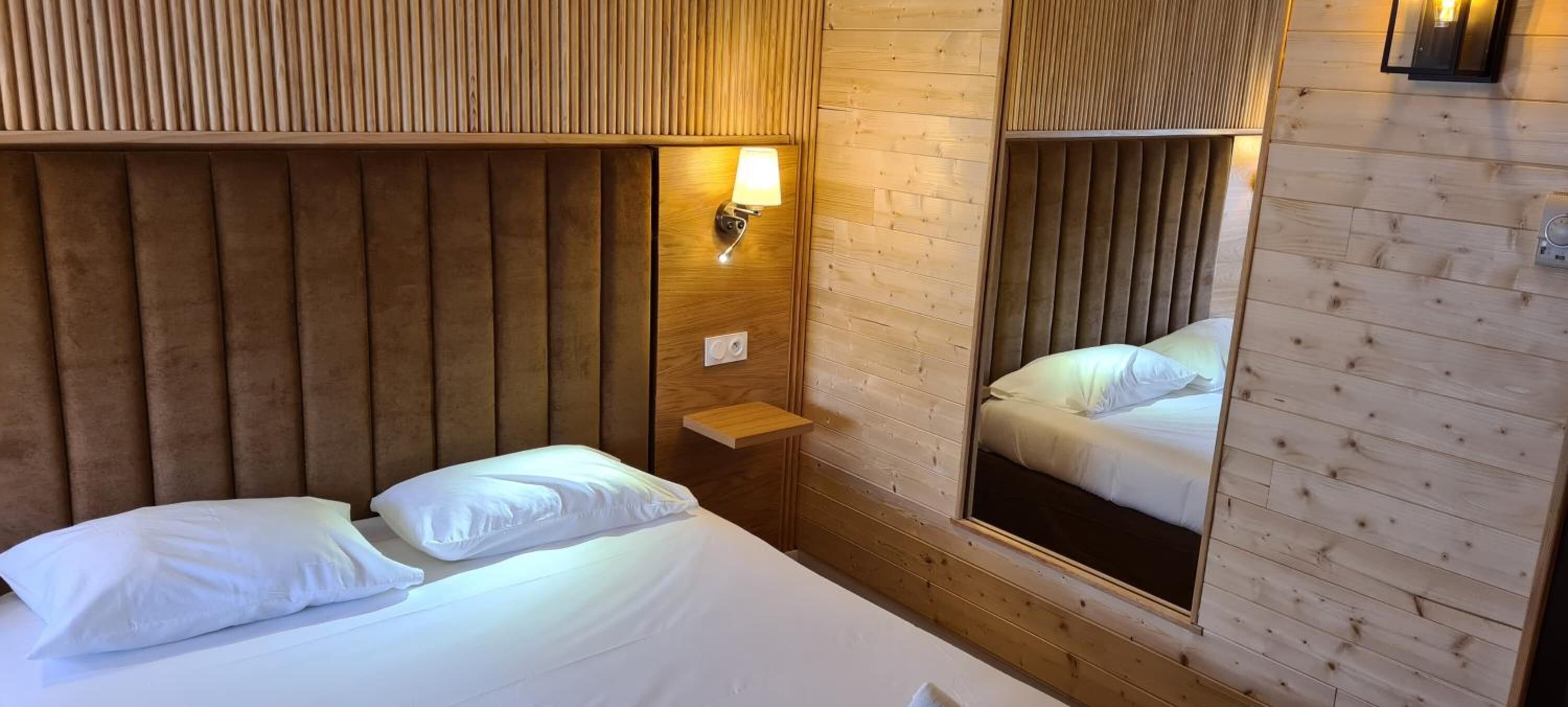 Un dormitorio con cabecera de madera, lámpara de noche, espejo y cama con ropa blanca.