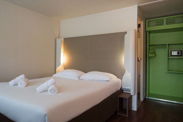 A hotel room with a large bed, two pillows, a nightstand, a green wall, and a door with a handle.