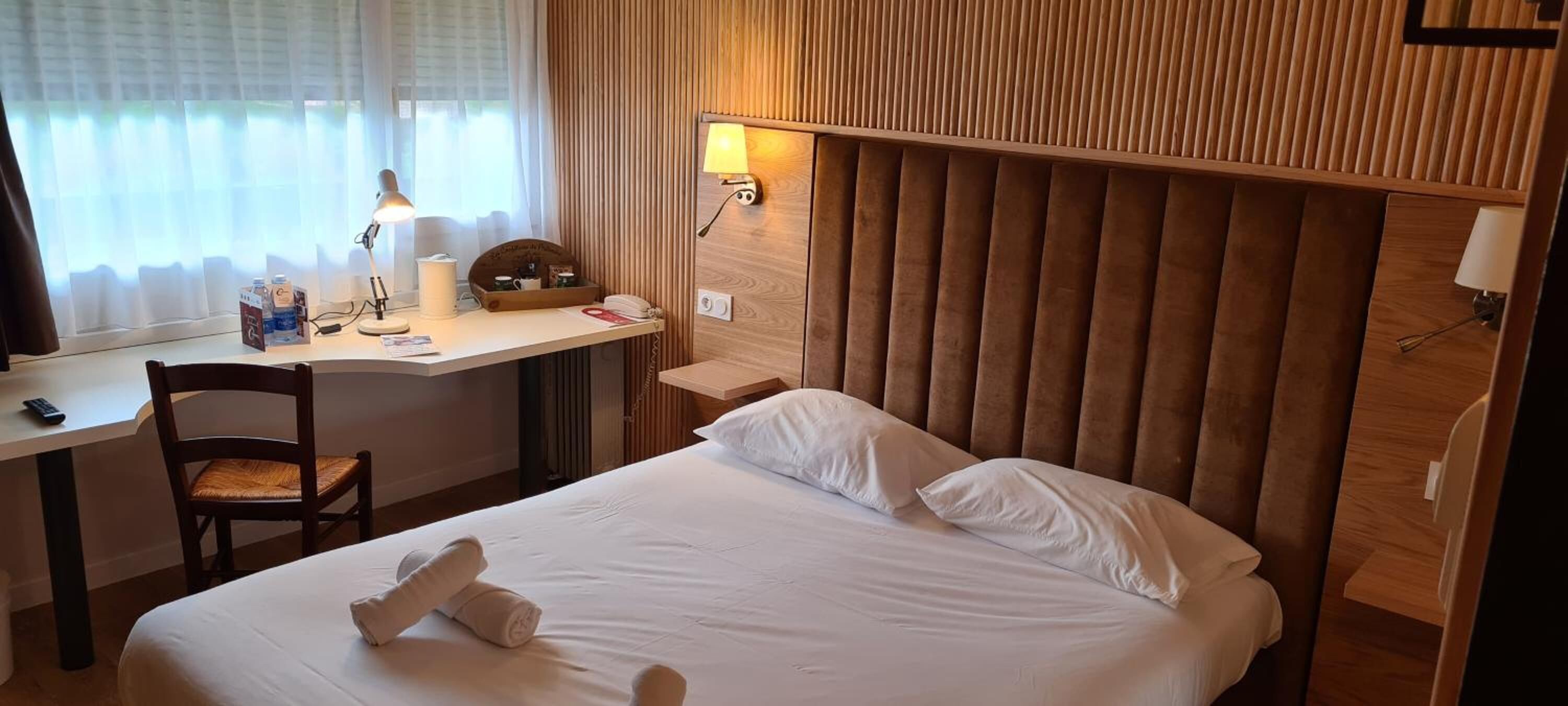 Una habitación de hotel con una cama, un escritorio, una silla, una lámpara y un teléfono en la pared.
