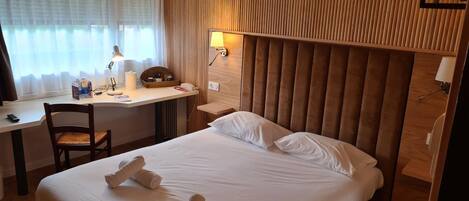 A hotel room with a bed, a desk, a chair, a lamp, and a wall-mounted phone.