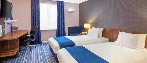 A hotel room with two beds, a desk, a chair, a TV, and a window with curtains.