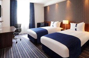A hotel room with two beds, a desk, a chair, and a window with curtains.