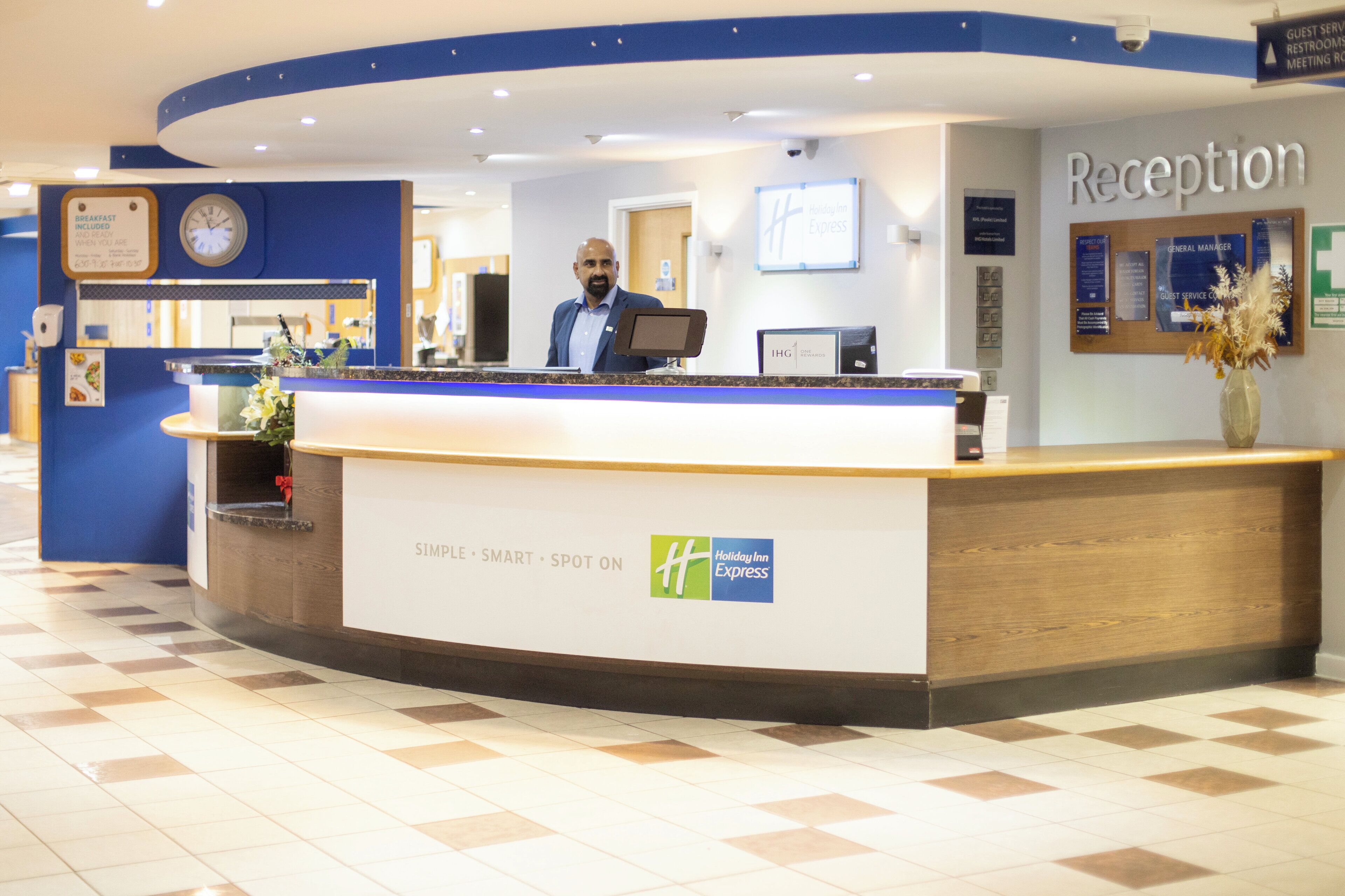 A Holiday Inn Express reception desk with a clock, a sign for guest services, and a reception area.