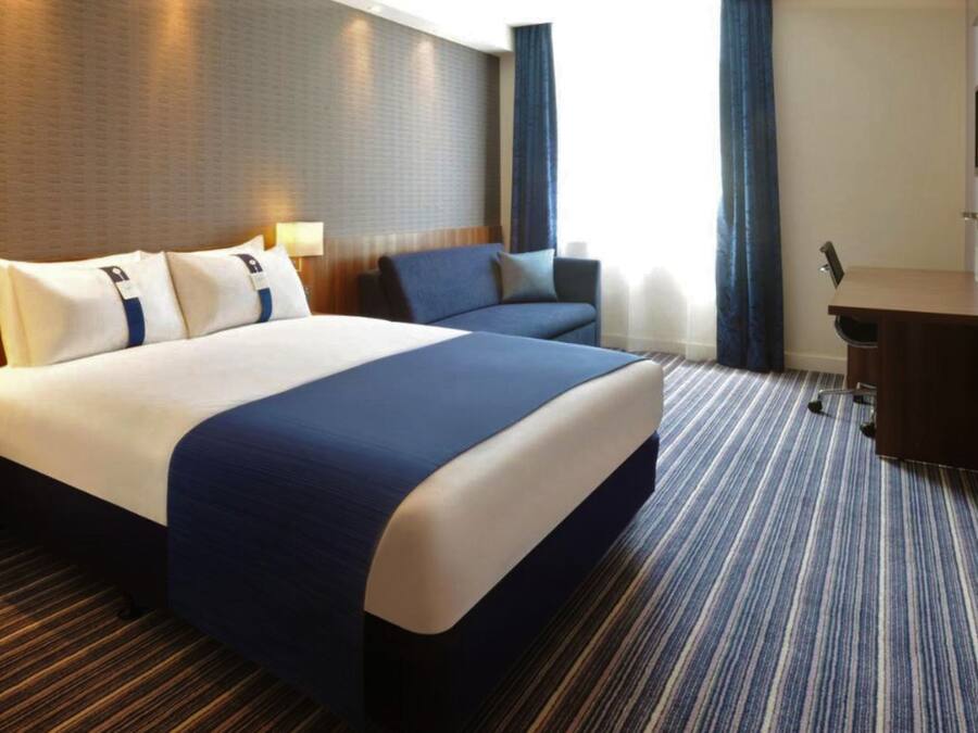 A hotel room with a large bed, a desk, and a chair.