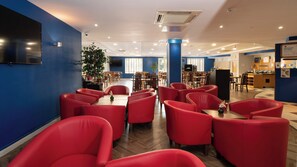 A modern dining area with red chairs, wooden tables, and a large plant.