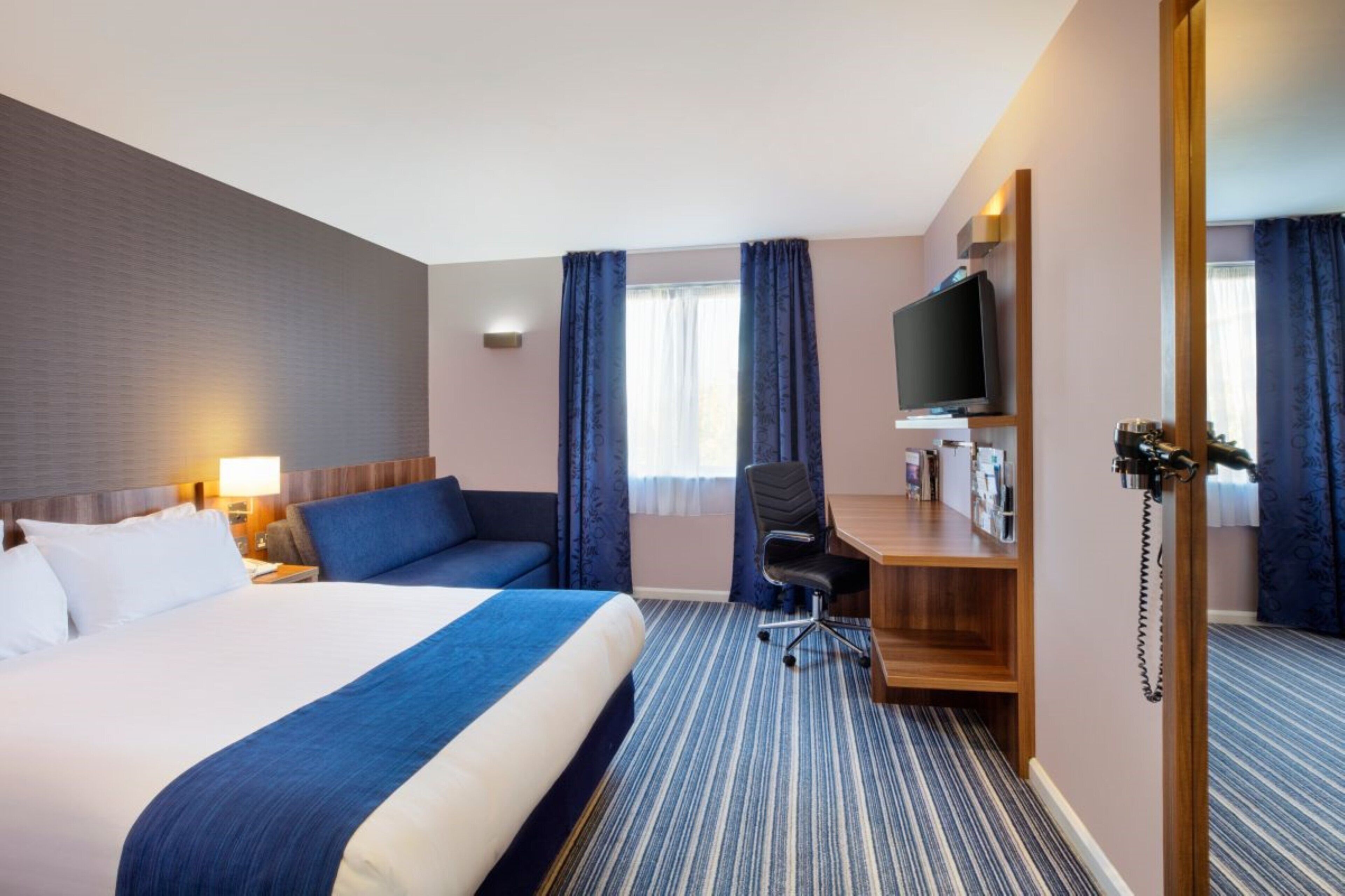 A hotel room with a large bed, a desk, a chair, a television, and a telephone.