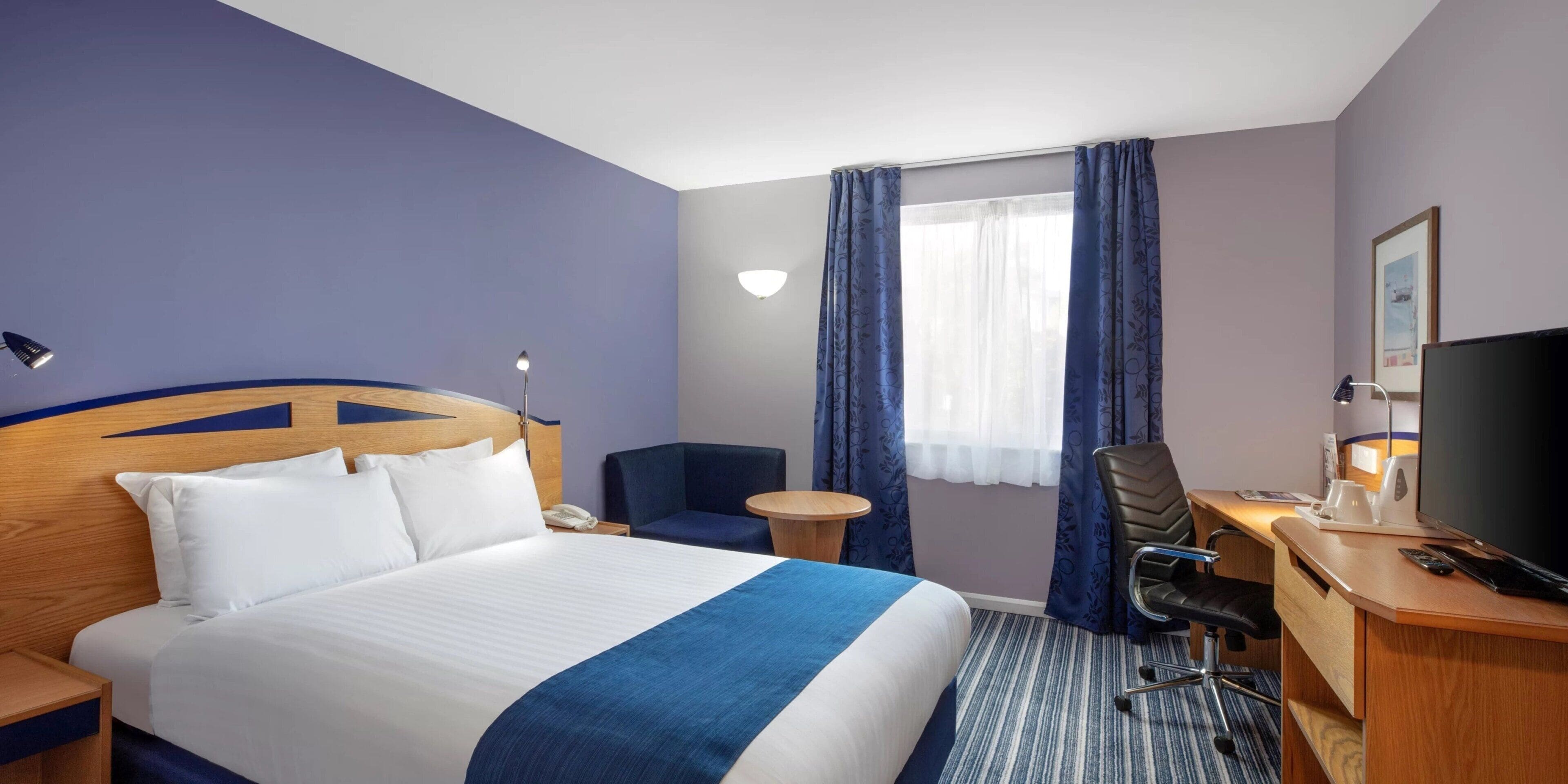 Una habitación de hotel con una cama grande, un escritorio con silla, un televisor y una ventana con cortinas.